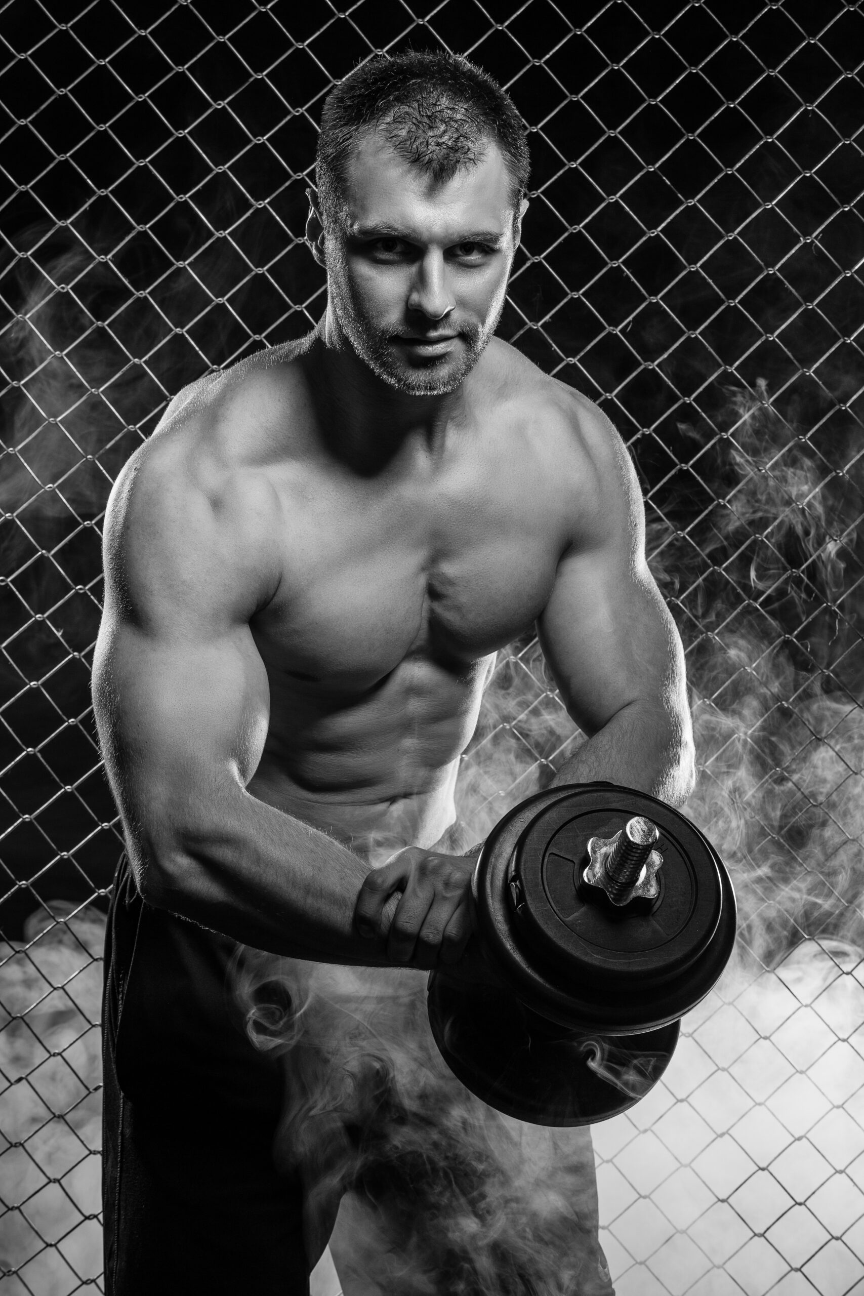 Beautiful, strong man with a dumbbell on fence background